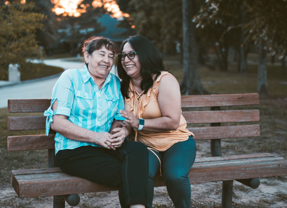 Dos mujeres sonriendo mientras están sentadas en un banco